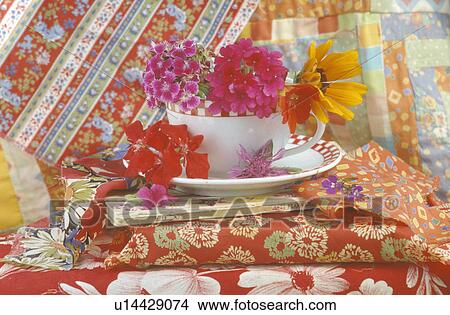 Still-life of pink and red with orange flowers in cup on pile of brightly coloured fabric View Large Photo Image Picture - Still-life of pink and red with orange flowers in cup on pile of brightly coloured fabric. Fotosearch