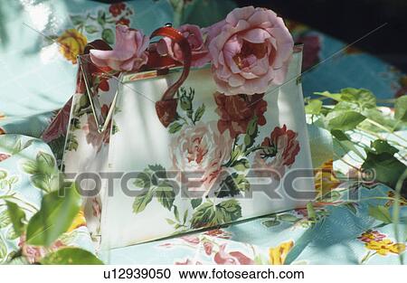 Stock Image - Still-life of pink roses on rose-patterned handbag . Fotosearch