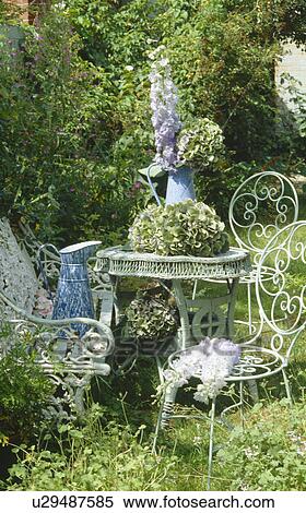 Still-life of white metal chairs and wicker table in green summer garden View Large Photo Image Stock Photography - Still-life of white metal chairs and wicker table in green summer garden. Fotosearch
