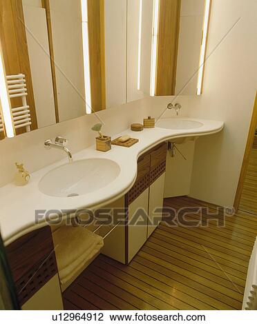 Stock Image - Strip lighting on mirror above basin in curved vanity unit. Fotosearch