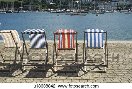 Stock Image - Striped deckchairs on paved quay at Dartmouth harbour in Devon. Fotosearch