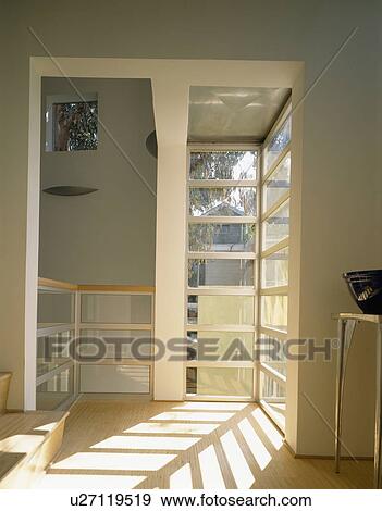 Stock Photo - Sunlight pouring through floor to ceiling windows in modern hall with wooden flooring. Fotosearch