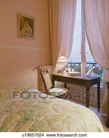 Picture - Table in front of window with pink curtains in pink bedroom with floral quilt on bed. Fotosearch