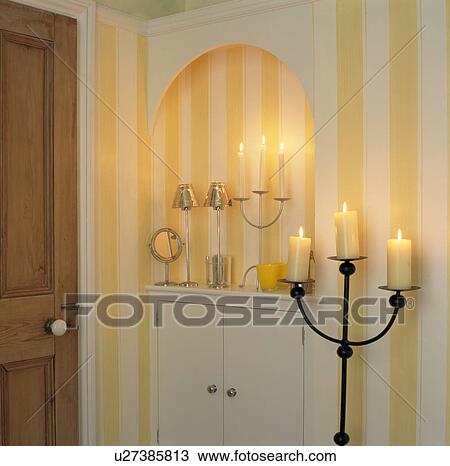 Stock Image - Tall candelabra with lighted candles in bathroom with yellow striped wallpaper. Fotosearch