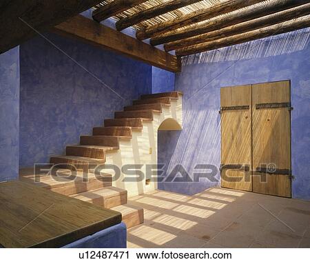 Stock Image - Textured blue walls in Mexican style hall with open staircase and wooden beams. Fotosearch