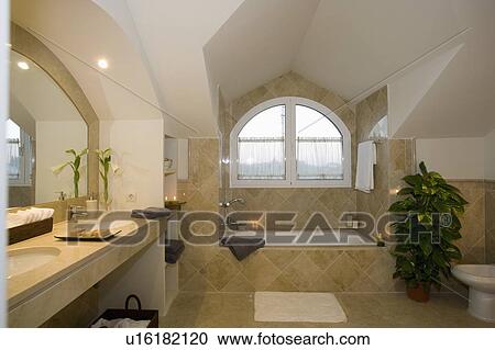 Stock Image - Tiled attic bathroom with unusual curved window and mirror in candlelight.. Fotosearch
