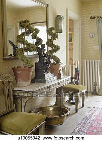 Stock Image - Topiary plants on console table in cream country hall. Fotosearch