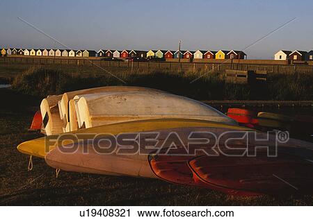 Stock Image - Upturned kayaks and boats on the beach with colourful beach huts in background at Southwold in Suffolk. Fotosearch