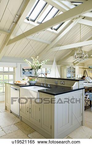 Stock Photography - White ceramic sink in pale grey fitted unit in modern openplan kitchen in converted coastal boathouse. Fotosearch