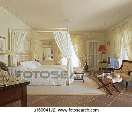 White Drapes On Modern Four Poster Bed Iin Spanish Bedroom Stock