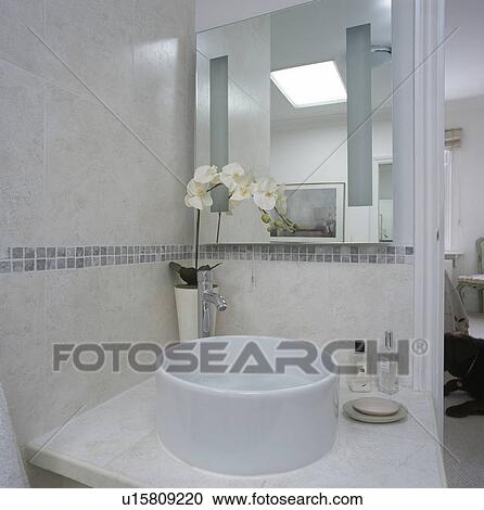 Stock Image - White orchid beside bowl basin on vanity unit in modern tiled bathroom. Fotosearch