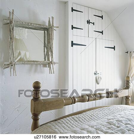 Stock Photograph - White twig framed mirror in white cottage bedroom with built in storage cupboards. Fotosearch