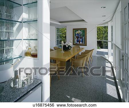 Stock Photograph - Wicker chairs and wooden table in modern white dining room with granite flooring. Fotosearch