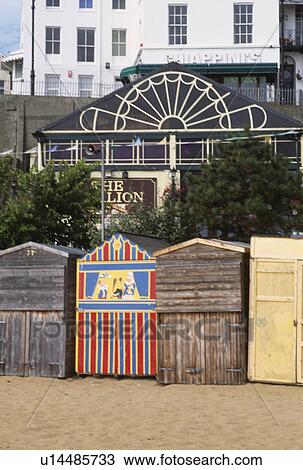 Stock Image - Wooden beach huts with painted Punch & Judy hut on the beach at Broadstairs in Kent. Fotosearch