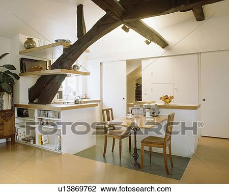Wooden table and chairs in modern white kitchen in attic conversion with shelving on large ached beam View Large Photo Image Stock Image - Wooden table and chairs in modern white kitchen in attic conversion with shelving on large ached beam. Fotosearch