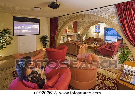 Stock Photo - Young woman relaxing in red armchair in television room in Spanish villa. Fotosearch