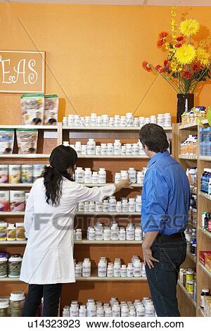 Stock Image - Back view of a female employee helping customer in drugstore. Fotosearch
