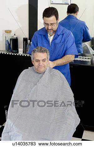Stock Image - Barber tying cloth before haircut of a mature man. Fotosearch