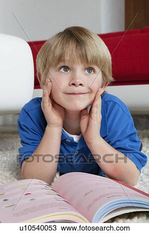 Blond boy lying down with book dreaming in house View Large Photo Image Stock Image - Blond boy lying down with book dreaming in house. Fotosearch