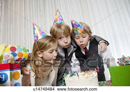 Picture - Brothers and sister blowing candles on birthday cake together. Fotosearch