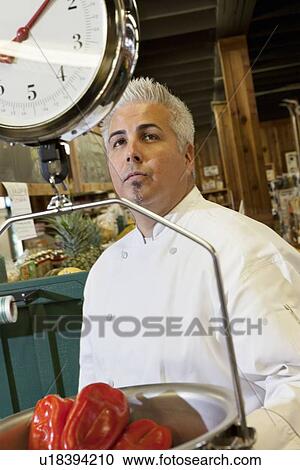 Stock Image - Chef looking at weighing scale with red bell pepper in market. Fotosearch