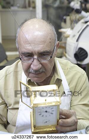 Stock Photo - Close-up of a mature man concentrating on repairing clock in workshop. Fotosearch