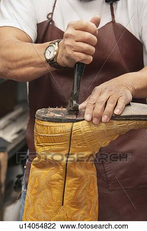 Stock Image - Close-up of skilled shoemaker's hands cutting shoe sole. Fotosearch
