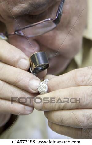 Stock Photograph - Cropped image of a mature worker looking through loupe at ring. Fotosearch