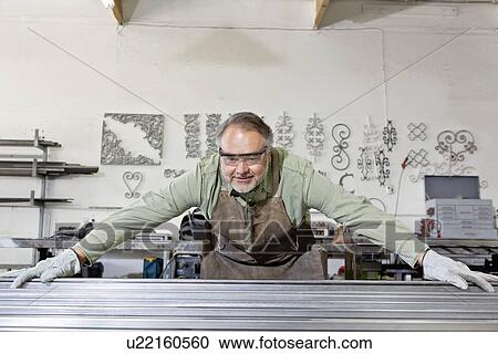 Stock Image - Front view of a mature metalworker wearing protective clothing while working in workshop. Fotosearch