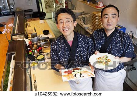 Stock Image - Happy chefs with prepared Asian cuisines in restaurant. Fotosearch