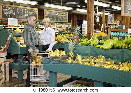 Stock Photograph - Happy couple standing with shopping cart in produce market. Fotosearch