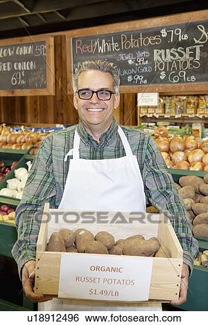 Stock Photograph - Happy mature employee carrying potato box in vegetable market. Fotosearch