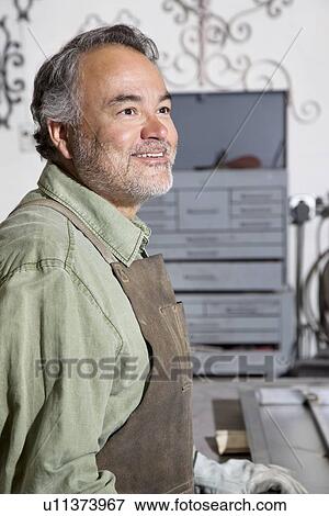 Stock Photo - Happy mature man looking away while standing in workshop. Fotosearch