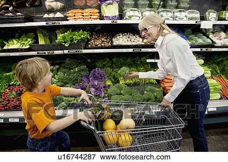 Happy woman selecting vegetable while boy with shopping cart looking in grocery market View Large Photo Image Stock Photo - Happy woman selecting vegetable while boy with shopping cart looking in grocery market. Fotosearch