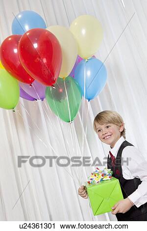 Stock Image - Happy young birthday boy with party balloon and gift looking away. Fotosearch