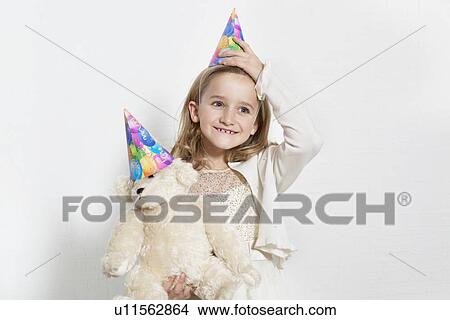 Picture - Happy young birthday girl wearing party hat with teddy bear over colored background. Fotosearch