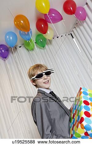 Happy young boy wearing sunglasses holding gift in party View Large Photo Image Stock Photo - Happy young boy wearing sunglasses holding gift in party. Fotosearch