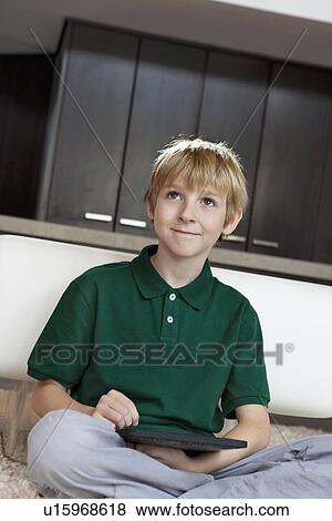Happy young boy with tablet pc sitting on rug View Large Photo Image Stock Photo - Happy young boy with tablet pc sitting on rug. Fotosearch
