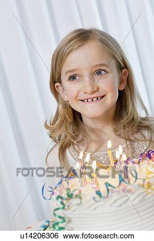 Stock Photograph - Happy young girl looking away with candles burning on birthday cake. Fotosearch