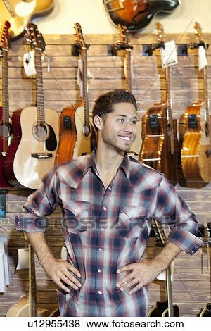 Stock Photo - Happy young music store owner with hands on hips standing in front of guitars. Fotosearch