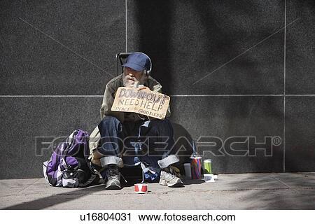 Stock Image - Homeless person sitting with a placard on sidewalk. Fotosearch