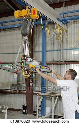 Stock Image - Industrial worker adjusting machinery in factory. Fotosearch