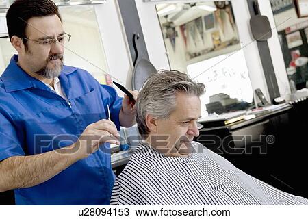 Stock Image - Mature barber giving a haircut to customer. Fotosearch