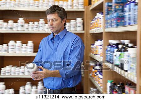 Mature man looking at pill bottle in drugstore View Large Photo Image Picture - Mature man looking at pill bottle in drugstore. Fotosearch