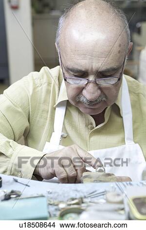 Mature skilled worker concentrating on repairing ring in workshop View Large Photo Image Picture - Mature skilled worker concentrating on repairing ring in workshop. Fotosearch