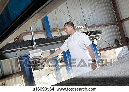 Picture - Mid adult industrial worker using machinery in factory. Fotosearch