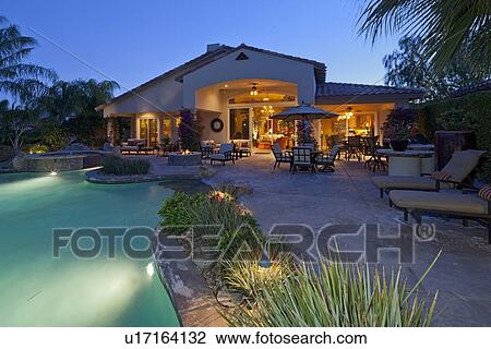 Stock Image - Patio with chaise lounge near swimming pool in manor house. Fotosearch