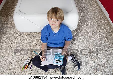 Picture - Portrait of a blond boy sitting near sofa doing homework. Fotosearch