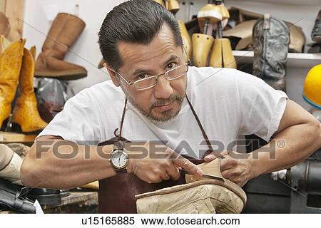 Stock Photography - Portrait of a confident shoemaker cutting sole from footwear in workshop. Fotosearch