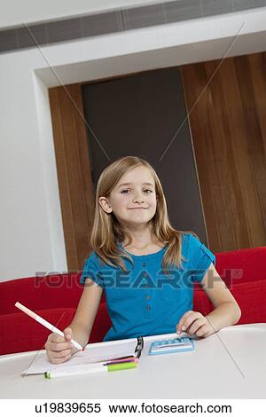 Stock Photography - Portrait of a happy girl doing homework at table. Fotosearch